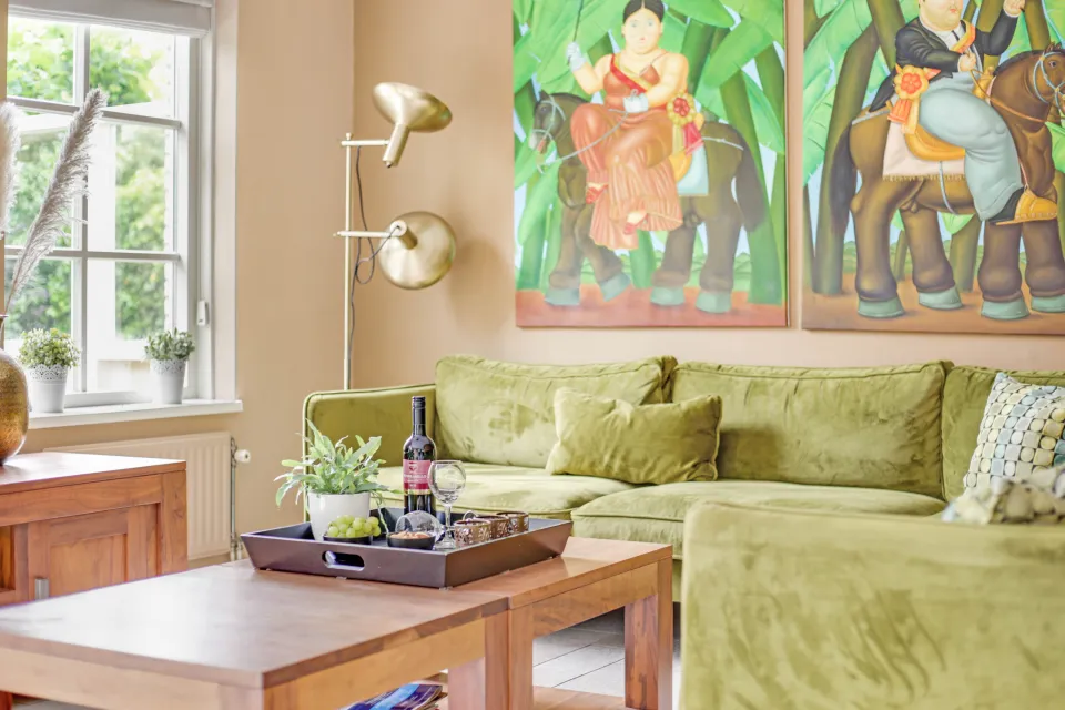 Woonkamer met groene hoekbank, houten salontafel en kleurrijke schilderijen