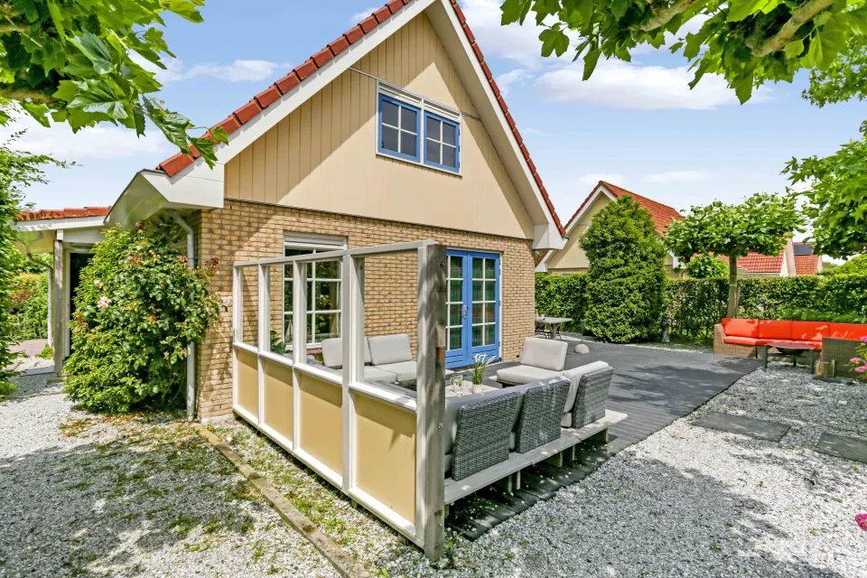Vakantiewoning met serre, blauwe kozijnen en een loungeset op het terras