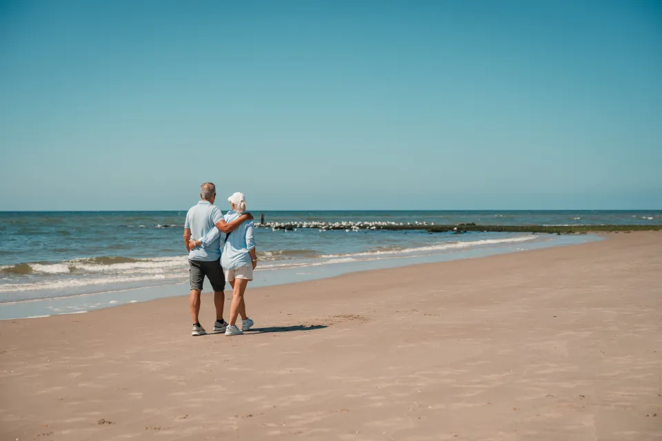 Ouder stel wandelt langs de vloedlijn met de zee en golfbrekers