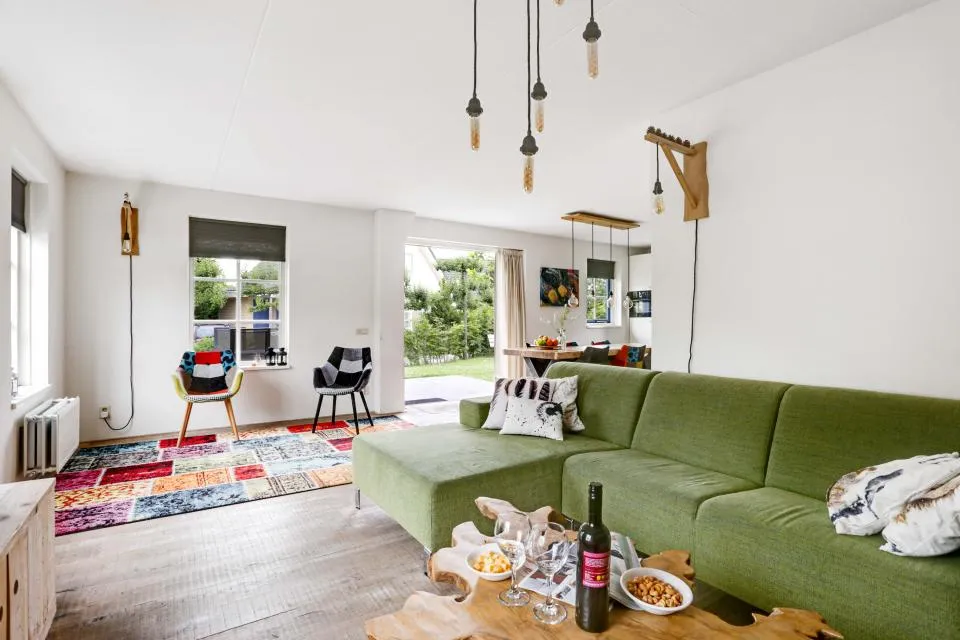 Woonkamer met groene bank, hanglampen en doorkijk naar de eethoek in een vakantiewoning