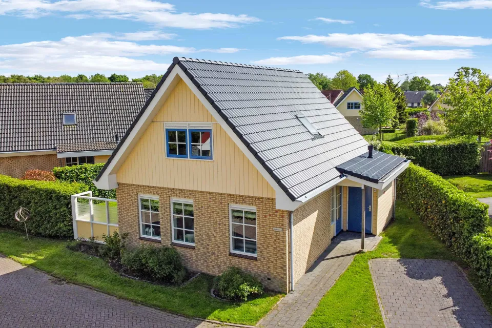 Luchtfoto van een vakantiewoning met grijs dak, terras en tuin met hagen op het park