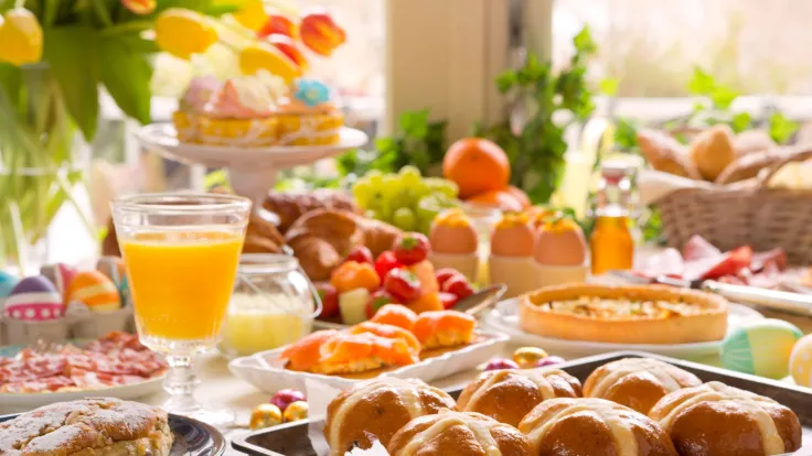 Rijk gedekte paastafel met broodjes, fruit, jus dorange en tulpen in het zonlicht