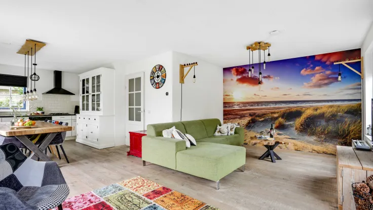 Woonkamer met groene bank, kleurrijk vloerkleed en fotobehang van het strand